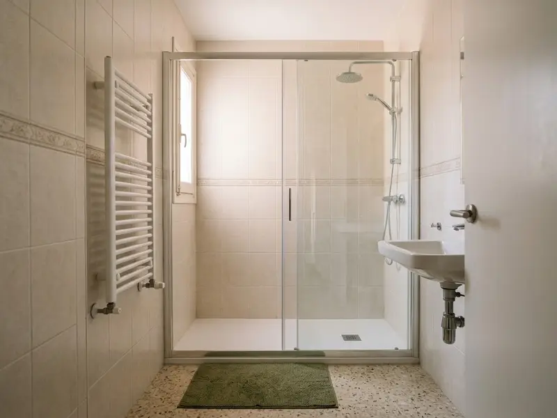 Mampara corredera de cristal transparente en una ducha con azulejo beige y cenefa